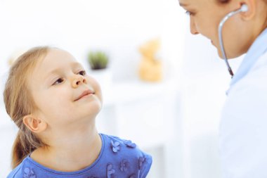 Doktor steteskopla küçük bir kızı muayene ediyor. Her zamanki tıbbi muayenede gülümseyen çocuk hasta. Tıp ve sağlık hizmetleri kavramları