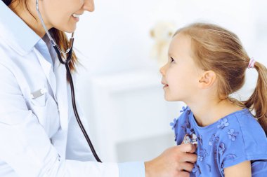 Doktor steteskopla küçük bir kızı muayene ediyor. Her zamanki tıbbi muayenede gülümseyen çocuk hasta. Tıp ve sağlık hizmetleri kavramları