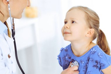 Doktor steteskopla küçük bir kızı muayene ediyor. Her zamanki tıbbi muayenede gülümseyen çocuk hasta. Tıp ve sağlık hizmetleri kavramları