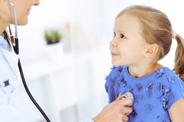 Doktor steteskopla küçük bir kızı muayene ediyor. Her zamanki tıbbi muayenede gülümseyen çocuk hasta. Tıp ve sağlık hizmetleri kavramları