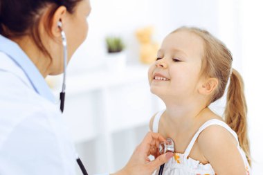 Doktor steteskopla küçük bir kızı muayene ediyor. Her zamanki tıbbi muayenede gülümseyen çocuk hasta. Tıp ve sağlık hizmetleri kavramları