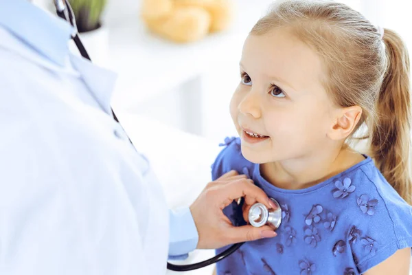 Arzt untersucht ein kleines Mädchen per Stethoskop. Glücklich lächelnder Kinderpatient bei der üblichen ärztlichen Untersuchung. Medizin- und Gesundheitskonzepte — Stockfoto