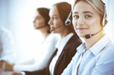 Çağrı merkezi ve iş adamları konsepti. Kulaklıklı, müşterilere danışan güzel bir iş kadını. Ofiste çalışan çeşitli telefon operatörleri