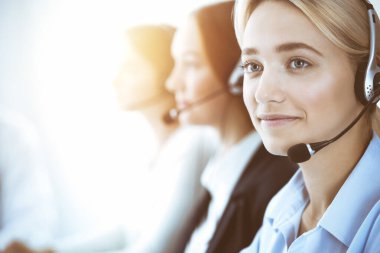 Çağrı merkezi ve iş adamları konsepti. Kulaklıklı, müşterilere danışan güzel bir iş kadını. Ofiste çalışan çeşitli telefon operatörleri