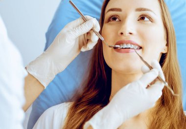 Diş hekiminde dişçi tarafından muayene edilen diş telleriyle gülümseyen genç bir kadın. Sağlıklı dişler ve tıbbi bakım konsepti