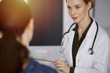 Neşeli gülümseyen kadın doktor ve hasta kadın güncel sağlık muayenesini güneşli klinikte otururken tartışıyorlar. Hastanede mükemmel bir tıbbi hizmet. Tıp konsepti