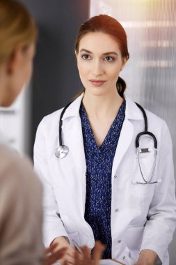 Neşeli gülümseyen kadın doktor ve hasta kadın güncel sağlık muayenesini güneşli klinikte otururken tartışıyorlar. Hastanede mükemmel bir tıbbi hizmet. Tıp konsepti