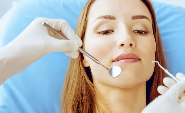 Lachende jonge vrouw met orthodontische haakjes onderzocht door tandarts in tandheelkundige kliniek. Gezonde tanden en medische zorg concept — Stockfoto