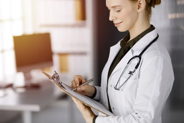 Allegro sorridente medico femminile utilizzando appunti in clinica soleggiata. Ritratto di donna medico amichevole al lavoro. Servizio medico perfetto in ospedale. Concetto di medicina — Foto Stock