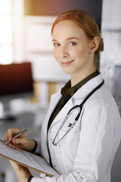 Allegro sorridente medico femminile utilizzando appunti in clinica soleggiata. Ritratto di donna medico amichevole al lavoro. Servizio medico perfetto in ospedale. Concetto di medicina — Foto Stock