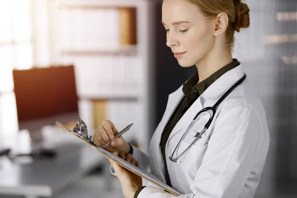 Allegro sorridente medico femminile utilizzando appunti in clinica soleggiata. Ritratto di donna medico amichevole al lavoro. Servizio medico perfetto in ospedale. Concetto di medicina — Foto Stock