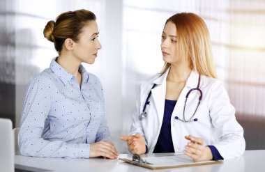 Genç, güzel kadın-doktor ve hastası bir klinikteki güneşli dolabın masasında birlikte otururken şu anki sağlık muayenesini tartışıyorlar. Kadın hekim bir şeyler yazıyor.