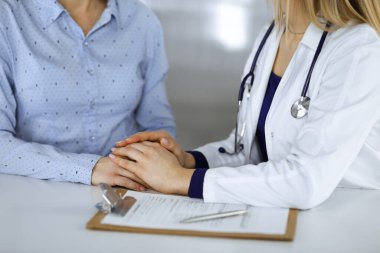 Bilinmeyen kadın doktor, bir klinikteki dolapta yan yana otururken hastasına güven vermek için elini tutuyor. Kadın doktor bir dosya ve steteskop kullanıyor. Kapat.