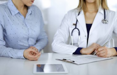 Bilinmeyen kadın. Doktor, klinikteki dolapta birlikte otururken hastasını dinliyor. Steteskoplu kadın doktor panoya yazı yazıyor, kapat. Mükemmel sağlık.