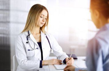 Genç, güzel kadın-doktor ve hastası bir klinikteki güneşli dolabın masasında birlikte otururken şu anki sağlık muayenesini tartışıyorlar. Kadın hekim bir şeyler yazıyor.