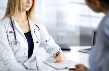 Bilinmeyen kadın doktor, bir klinikteki dolapta otururken hastasına bazı antibiyotikler yazıyor. Steteskoplu kadın doktor panoya yazı yazıyor, kapat