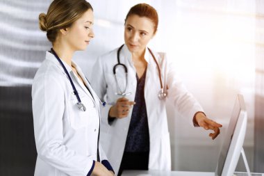 İki kadın doktor güneşli bir klinikte masada dururken tıbbi terapiyi tartışıyorlar. Doktorlar işte bilgisayar kullanırlar. Tıpta takım çalışması. Tıp konsepti
