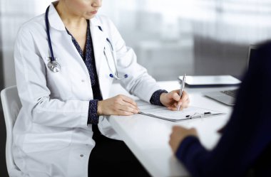 Bilinmeyen kadın-doktor, bir klinikteki dolapta birlikte otururken hastasına bazı tıbbi tavsiyeler yazıyor. Hekim bir dosya kullanıyor, yakın plan. Mükemmel.