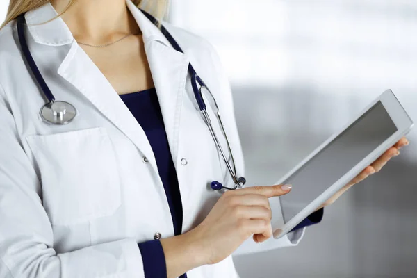 신원을 알 수없는 여성 - 의사가 진료소 캐비닛에 서 있는 동안 손에 태블릿 컴퓨터를 들고 있다. 여성 의사가 일하고 있고, 클로즈업중입니다. 병원에서의 완벽 한 의료 서비스. 의학적 개념 — 스톡 사진