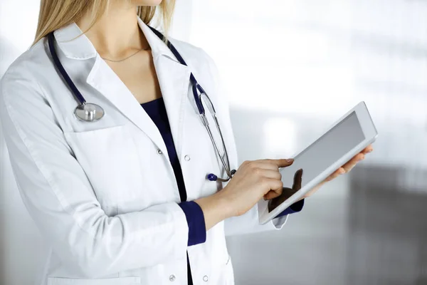 신원을 알 수없는 여성 - 의사가 진료소 캐비닛에 서 있는 동안 손에 태블릿 컴퓨터를 들고 있다. 여성 의사가 일하고 있고, 클로즈업중입니다. 병원에서의 완벽 한 의료 서비스. 의학적 개념 — 스톡 사진
