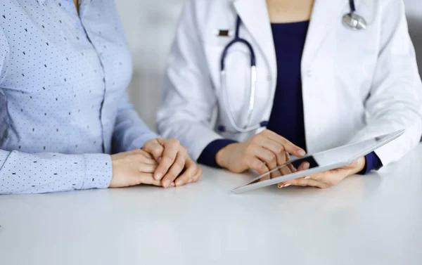 Bilinmeyen kadın-doktor, bir klinikteki dolapta birlikte otururken hastasına bir ilaç tarifi gösteriyor. Kadın hekim bilgisayar tableti ve steteskop kullanıyor.
