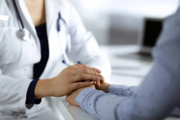 Neznámá žena-doktorka drží své pacienty za ruce a diskutuje o aktuálním zdravotním vyšetření, zatímco sedí za stolem ve skříni na klinice. Lékař se stetoskopem v práci, zblízka — Stock fotografie