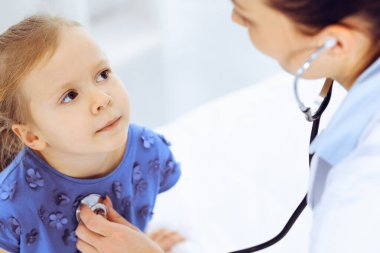 Doktor steteskopla küçük bir kızı muayene ediyor. Her zamanki tıbbi muayenede gülümseyen çocuk hasta. Tıp ve sağlık hizmetleri kavramları
