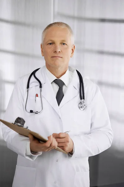 Ältere selbstbewusste Ärztin, die gerade steht und Klemmbrett in der Klinik benutzt. Perfekte medizinische Versorgung. Medizin und Gesundheitskonzept — Stockfoto