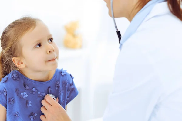 Arzt untersucht ein kleines Mädchen per Stethoskop. Glücklich lächelnder Kinderpatient bei der üblichen ärztlichen Untersuchung. Medizin- und Gesundheitskonzepte — Stockfoto