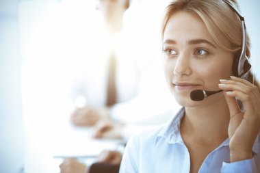 Çağrı merkezi ve iş adamları konsepti. Kulaklıklı, müşterilere danışan güzel bir iş kadını. Ofiste çalışan çeşitli telefon operatörleri