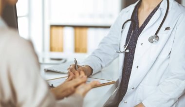 Doktor ve hasta klinikte otururken sağlık muayenesini tartışıyorlar. Hastanede mükemmel bir tıbbi hizmet.