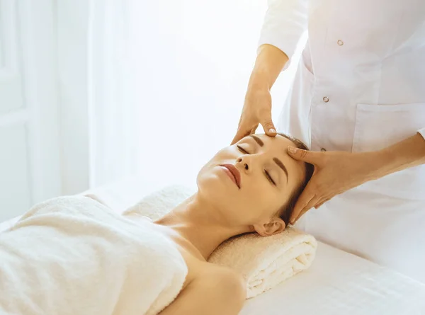 Piękna kobieta korzystająca z masażu twarzy z zamkniętymi oczami w słonecznym centrum spa. Relaksująca koncepcja leczenia w medycynie — Zdjęcie stockowe