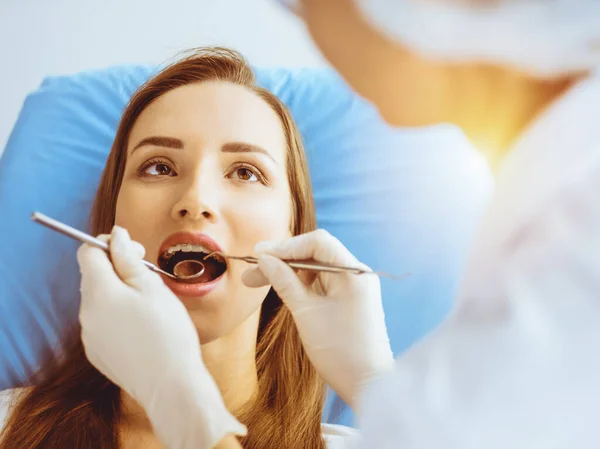 Uśmiechnięta młoda kobieta z nawiasami ortodontycznymi badana przez dentystę w słonecznej klinice dentystycznej. Zdrowe zęby i koncepcja medycyny — Zdjęcie stockowe