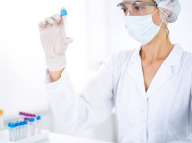 Koruyucu gözlüklü profesyonel kadın bilim adamı laboratuarda reaktörlerle araştırma tüpü kullanıyor. Tıp ve bilim araştırmaları kavramları