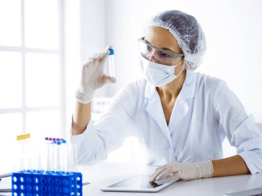 Koruyucu gözlüklü profesyonel kadın bilim adamı laboratuarda reaktörlerle araştırma tüpü kullanıyor. Tıp ve bilim araştırmaları kavramları