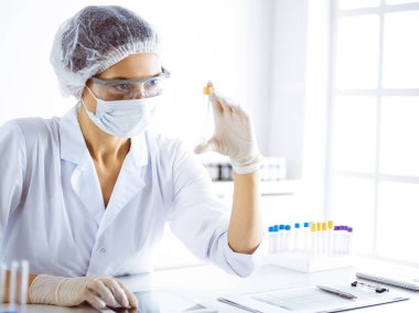 Koruyucu gözlüklü profesyonel kadın bilim adamı laboratuarda reaktörlerle araştırma tüpü kullanıyor. Tıp ve bilim araştırmaları kavramları