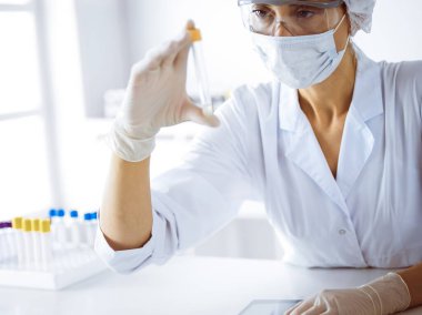 Koruyucu gözlüklü profesyonel kadın bilim adamı laboratuarda reaktörlerle araştırma tüpü kullanıyor. Tıp ve bilim araştırmaları kavramları