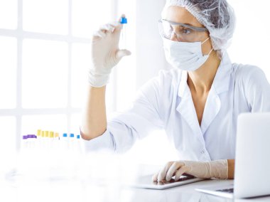 Koruyucu gözlüklü profesyonel kadın bilim adamı laboratuarda reaktörlerle araştırma tüpü kullanıyor. Tıp ve bilim araştırmaları kavramları