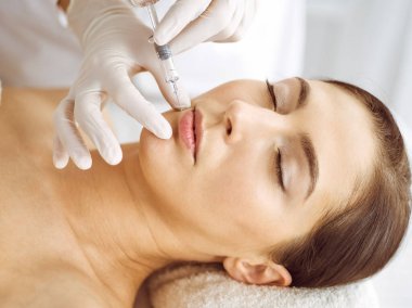 Güzellik uzmanı, genç esmer kadının yüzüne şırıngayla güzellik prosedürü uyguluyor. Kozmetik ilaç ve ameliyat, güzellik iğneleri.