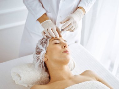 Güzellik uzmanı, genç esmer kadının yüzüne şırıngayla güzellik prosedürü uyguluyor. Kozmetik ilaç ve ameliyat, güzellik iğneleri.