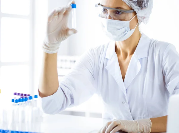 Professionele vrouwelijke wetenschapper in beschermende bril onderzoeken buis met reagentia in het laboratorium. Begrippen geneeskunde en wetenschappelijk onderzoek — Stockfoto