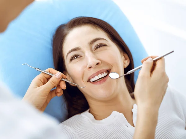 Lachende brunette vrouw wordt onderzocht door tandarts in de tandheelkundige kliniek. Handen van een arts met tandheelkundige instrumenten in de buurt van de mond van patiënten. Gezonde tanden en geneeskundeconcept — Stockfoto