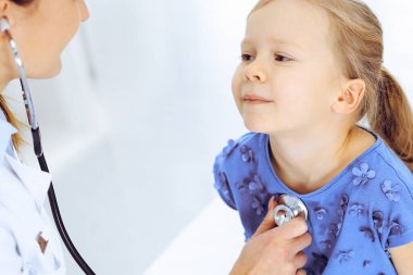 Doktor steteskopla küçük bir kızı muayene ediyor. Her zamanki tıbbi muayenede gülümseyen çocuk hasta. Tıp ve sağlık hizmetleri kavramları
