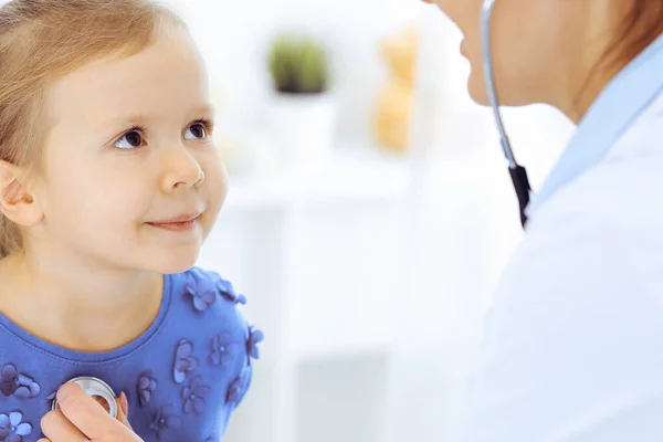 Arzt untersucht ein kleines Mädchen per Stethoskop. Glücklich lächelnder Kinderpatient bei der üblichen ärztlichen Untersuchung. Medizin- und Gesundheitskonzepte — Stockfoto