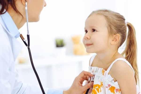 Doctor examinando a una niña por estetoscopio. Feliz niño sonriente paciente en la inspección médica habitual. Medicina y conceptos sanitarios —  Fotos de Stock