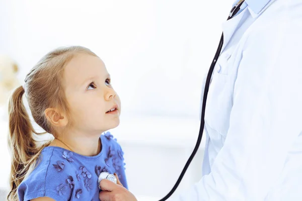 Arzt untersucht ein kleines Mädchen per Stethoskop. Glücklich lächelnder Kinderpatient bei der üblichen ärztlichen Untersuchung. Medizin- und Gesundheitskonzepte — Stockfoto