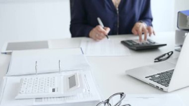 Beyaz hesap makinesini, işyerindeki vergileri, klasörü ve masasındaki gözlükleri hesaplayan iş kadınının karşısındaki mali belgelerin üzerine kapatın. Denetim ve vergi kavramı.