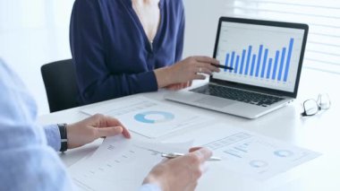 İş arkadaşları bir proje üzerinde işbirliği yapıyor, bir dizüstü bilgisayardaki mali verileri analiz ediyor ve bulguları tartışırken önemli veri noktalarına işaret ediyorlar. İş adamları, finans kavramı