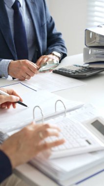 Ekonomik belgeleri analiz eden, hesap makineleri ve dizüstü bilgisayarlar kullanan iş adamları modern ofiste proje üzerinde birlikte çalışıyorlar. Denetim ve vergi kavramı.