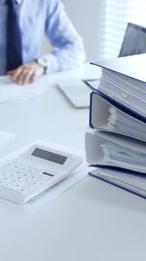 Ofis çalışanları mali raporları analiz ediyor ve ön planda evrak dolu mavi dosyalarla dolu beyaz bir masada otururken belgeleri imzalıyorlar. İş dünyasında denetim ve vergi teması